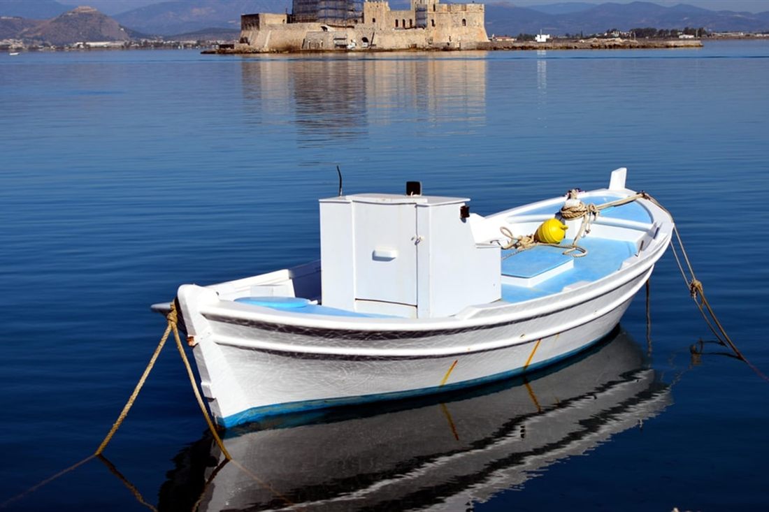 The Bourtzi castle on its islet in the bay of Nafplio, with a small white boat moored in calm blue water, seen on a Nafplio private tour.