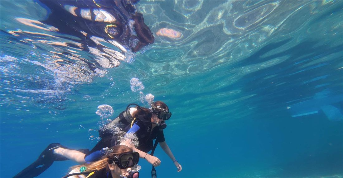 Two divers in masks swimming just below the surface in clear blue water off Tolo
