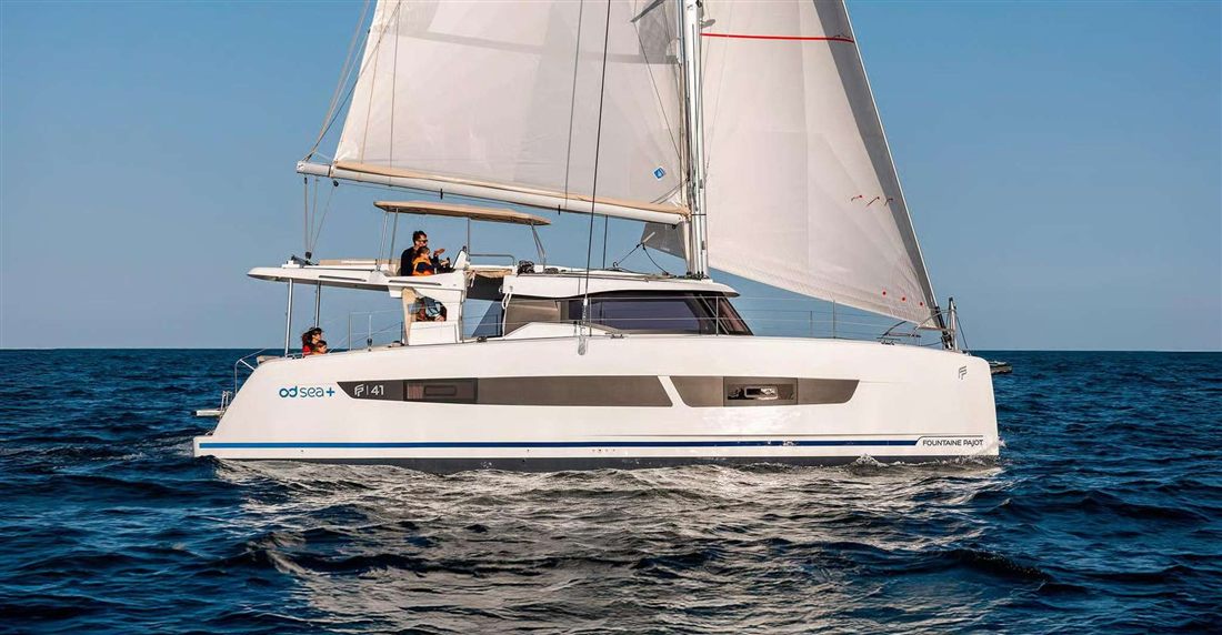 A white sailing catamaran under full sail on a deep blue sea