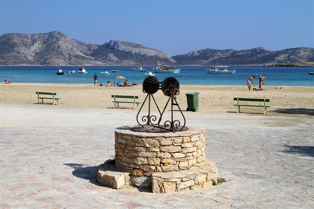A stone well on the beachfront of Koufonisi, with sand, sea and the hills of the Small Cyclades behind.