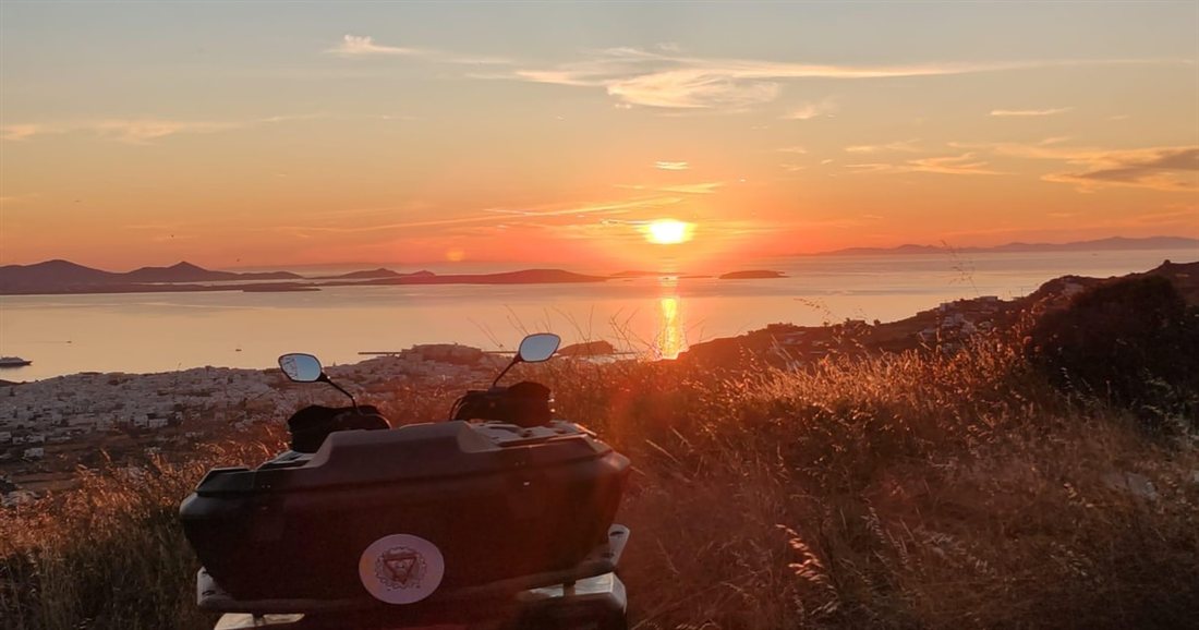 A quad bike on a hillside at sunset, with the sun going down over the sea and islands, on the sunset route of a Naxos ATV tour.