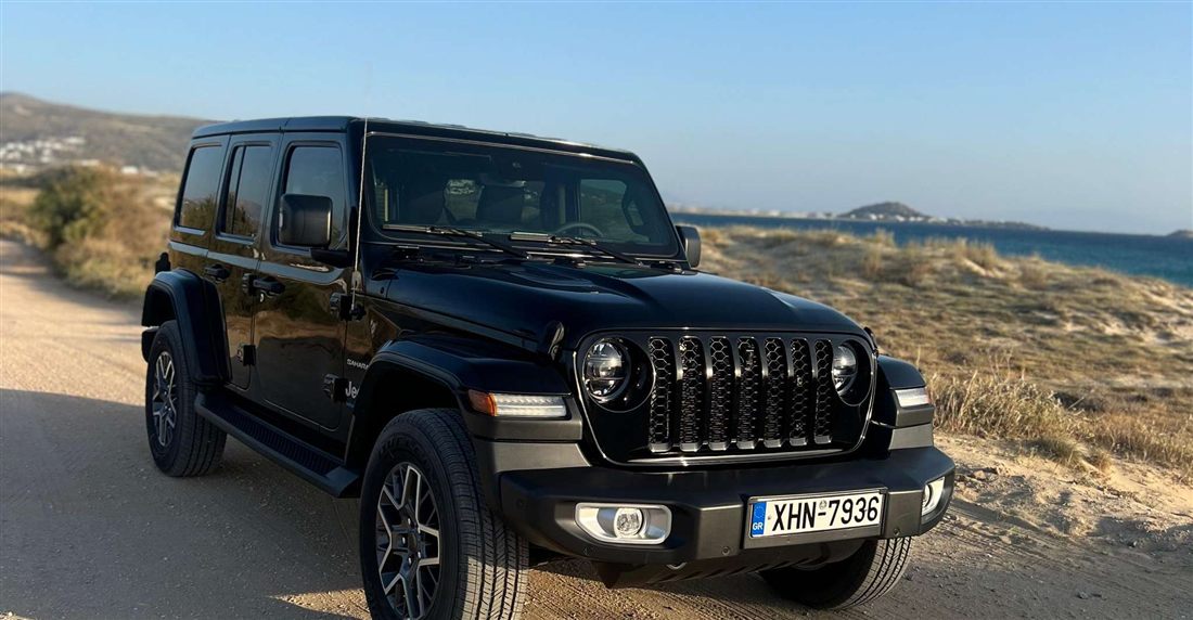 A black Jeep Wrangler on a sandy track above the sea and dunes on the coast of Naxos