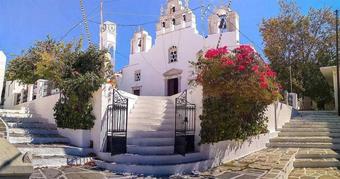 A white church with a bell tower and marble steps beside pink bougainvillea in a Naxos village, on a Naxos private tour.