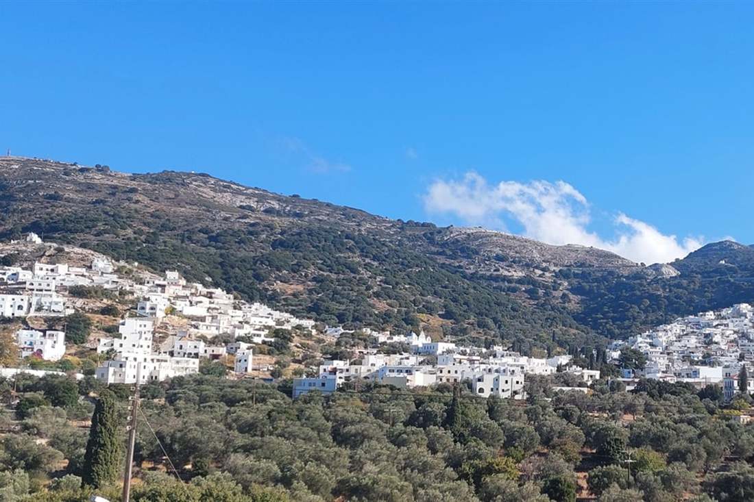 A white mountain village spread across a green hillside below rocky peaks, seen on a Naxos private tour.