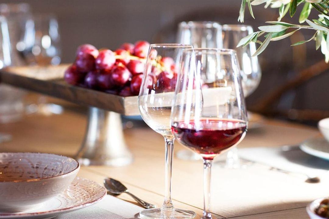 Glasses of red Agiorgitiko wine on a tasting table beside a stand of red grapes and an olive branch.