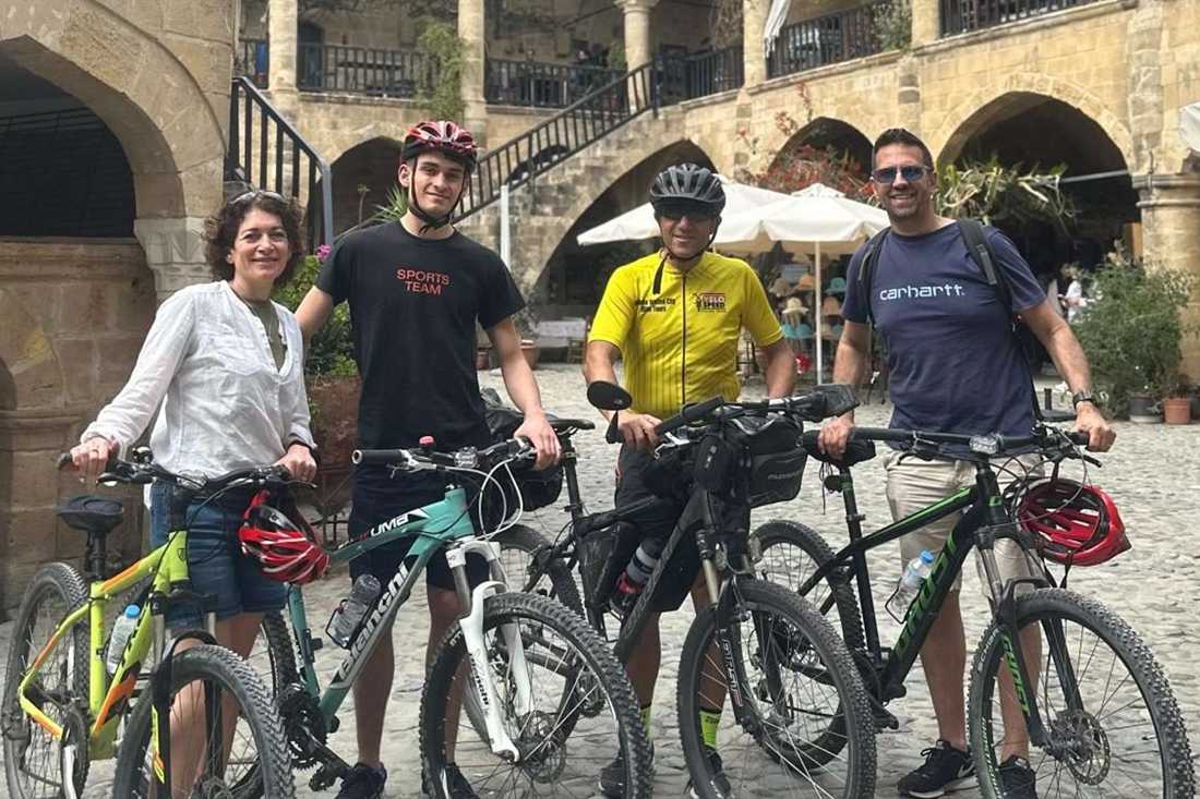 Four cyclists in helmets stand beside their bicycles in a cobbled courtyard under stone arches