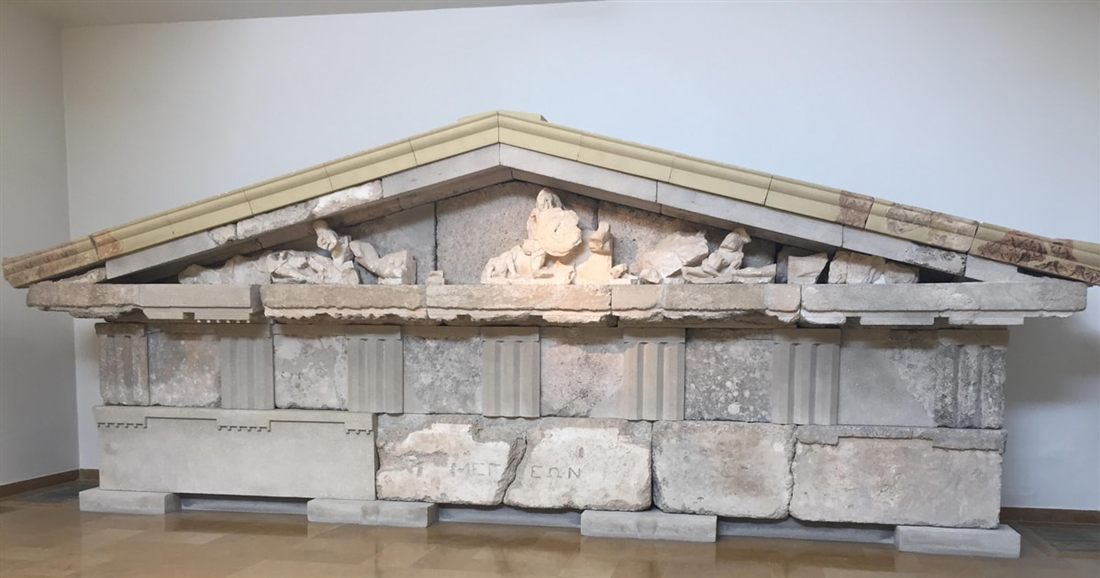 A reconstructed marble temple pediment with carved figures on display in a bright museum hall at Olympia.
