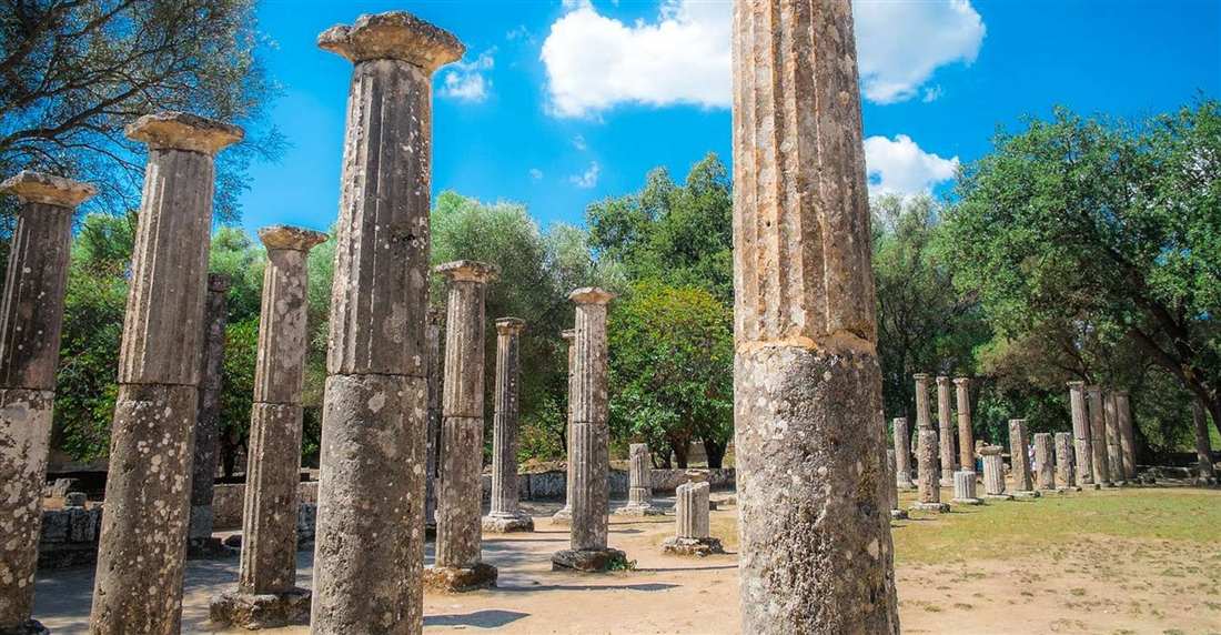 The columns of the palaestra at Ancient Olympia under a blue sky among green trees