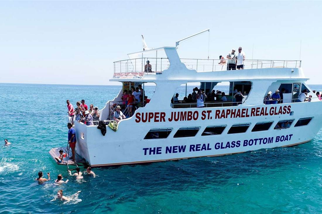 A large glass-bottom boat anchored off Paphos while passengers swim in the blue sea