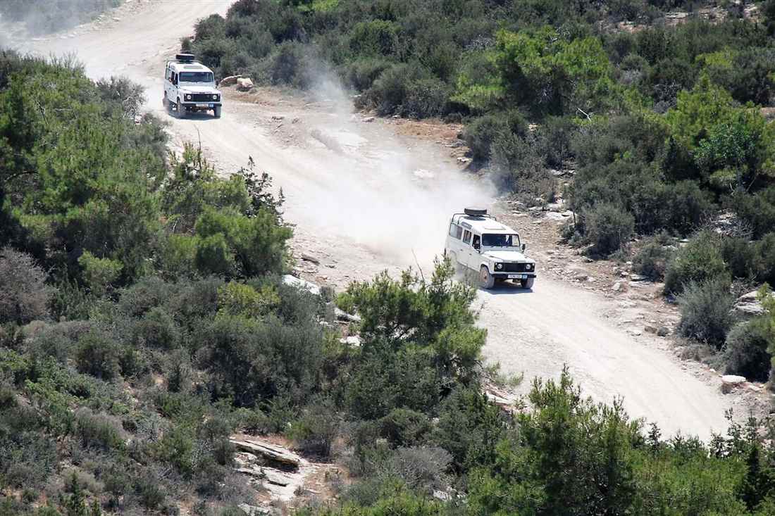 Two Land Rover jeeps raise dust on a dirt track through the green scrub of the Akamas peninsula
