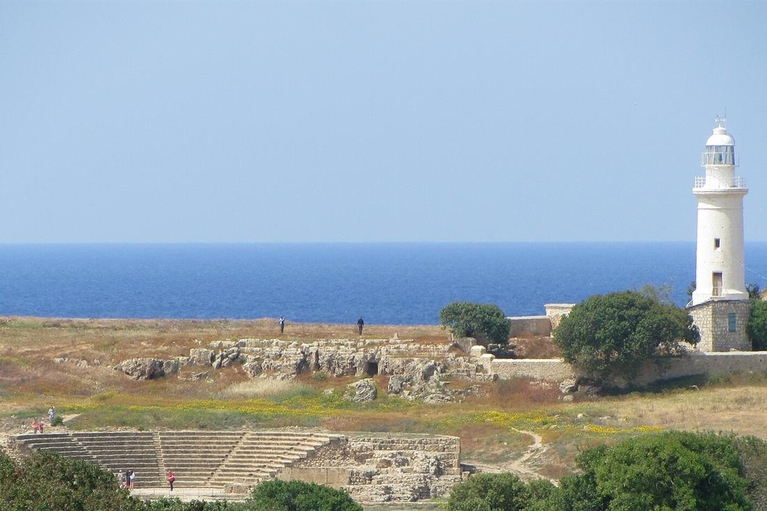 White lighthouse beside the sea with the ruins of a small amphitheatre below it