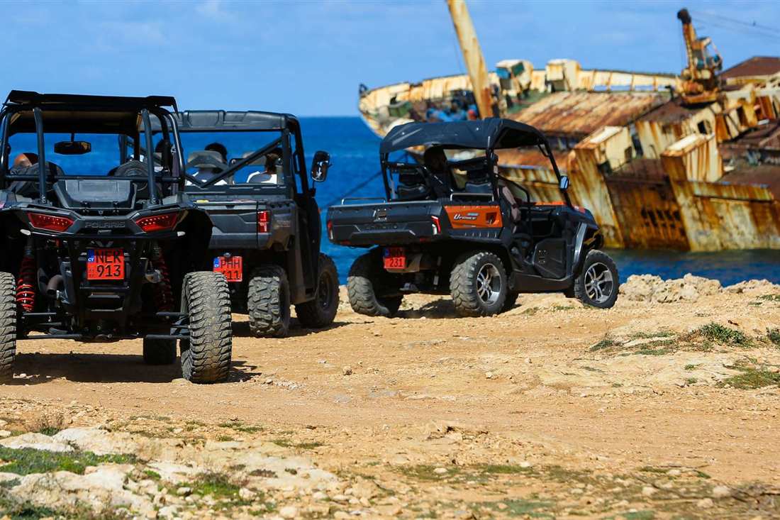Three off-road buggies parked on a rocky clifftop beside the rusty Edro III shipwreck and the blue sea