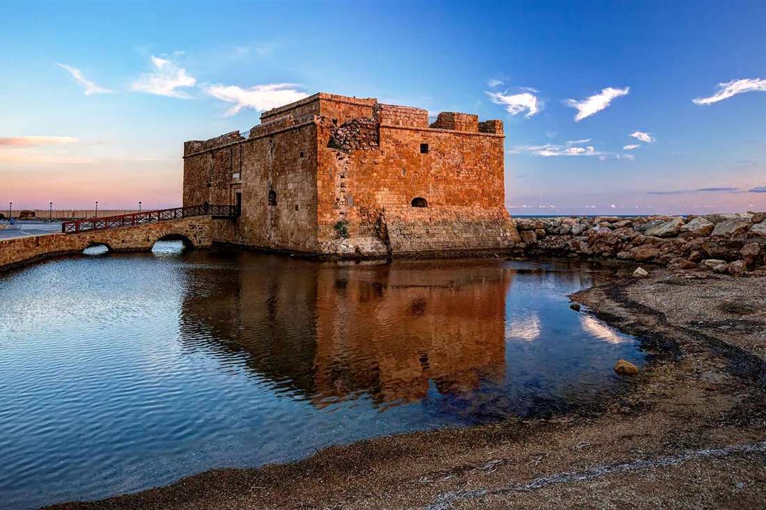The medieval fort of Paphos harbour reflected in calm water under a blue sky