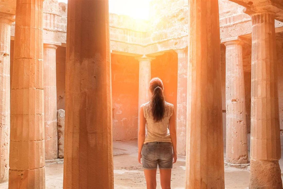 A visitor stands among the Doric columns of an underground courtyard tomb at the Tombs of the Kings in Paphos