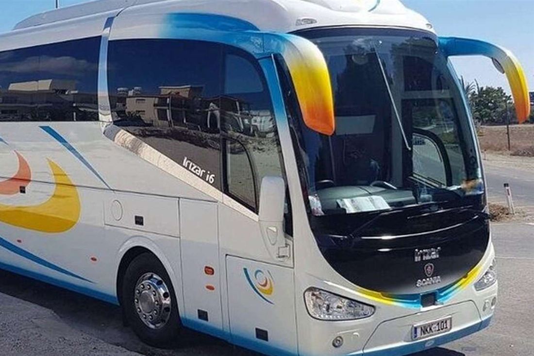 White coach with blue, yellow and orange stripes and a Cyprus number plate parked on a road in sunshine