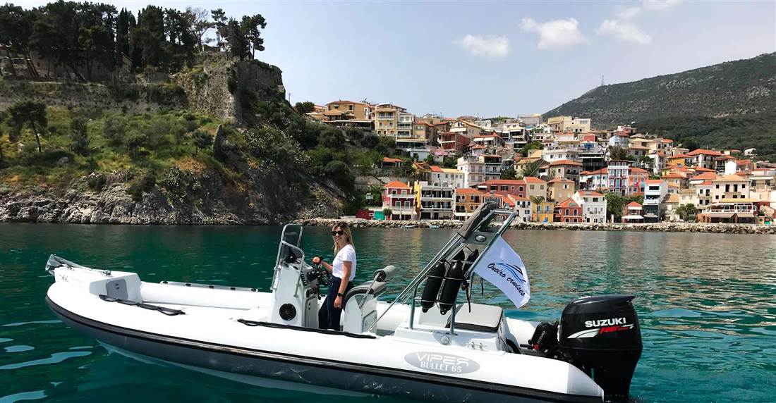 A white motor boat in the bay of Parga below the castle hill and the colourful houses of the town