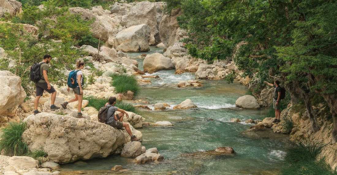 Hikers with backpacks crossing rocks in a clear mountain river inside a green gorge