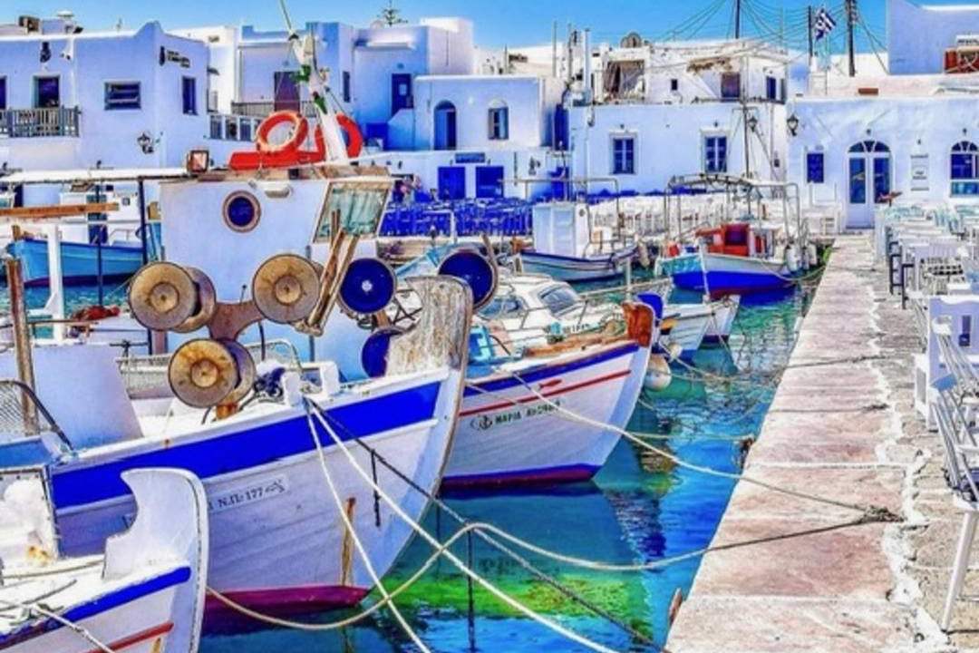 Fishing boats moored along the stone quay of the old harbour in Naoussa on Paros, with whitewashed houses behind.