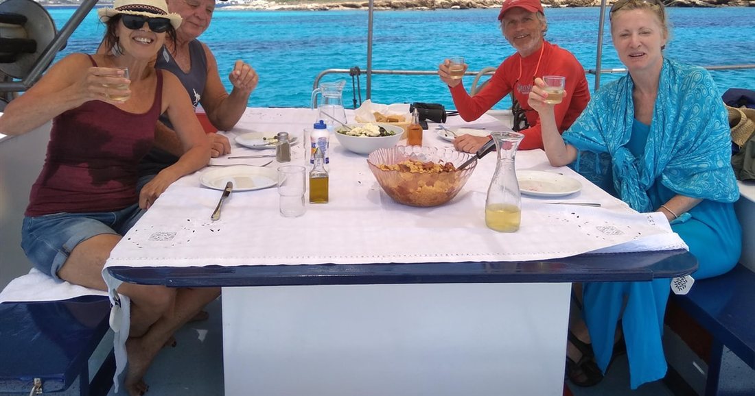 Guests at a table set with salad, bread and drinks on the deck of a boat, the lunch stop on a Paros fishing trip.