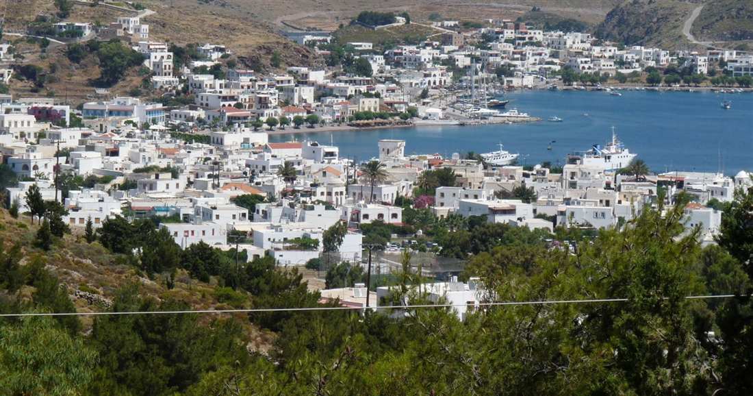 The harbour town of Skala on Patmos seen from the hillside, with white houses around a blue bay and moored boats.