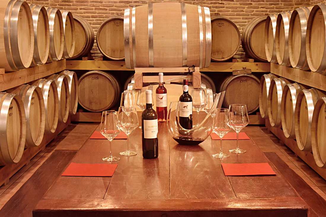 Wine glasses and bottles on a long tasting table between stacked oak barrels in a winery cellar