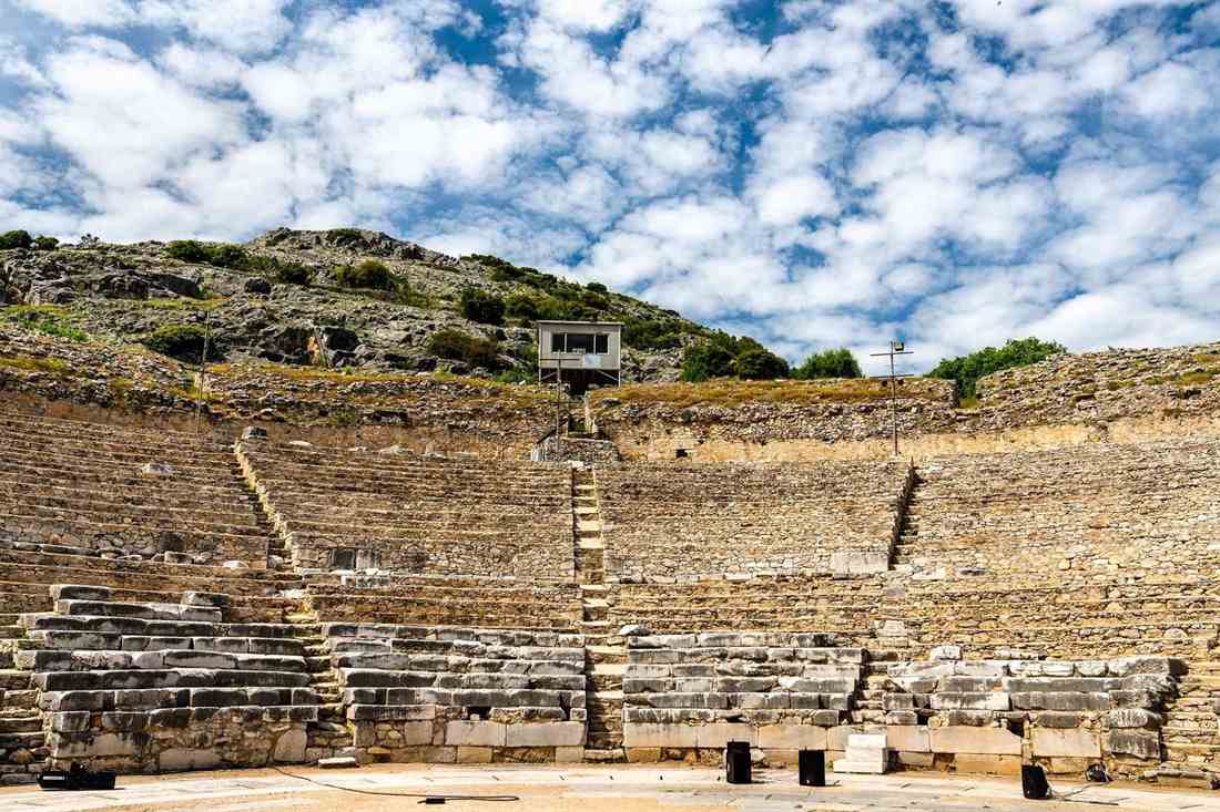 Stone seats of the ancient theatre of Philippi seen from the orchestra under a blue sky with white clouds