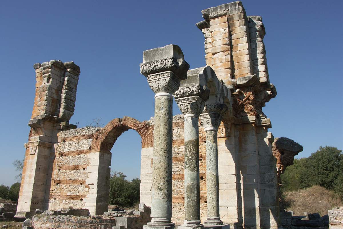 The standing pillars and brick arch of Basilica B at Philippi under a blue sky, part of the site that Philippi tickets open