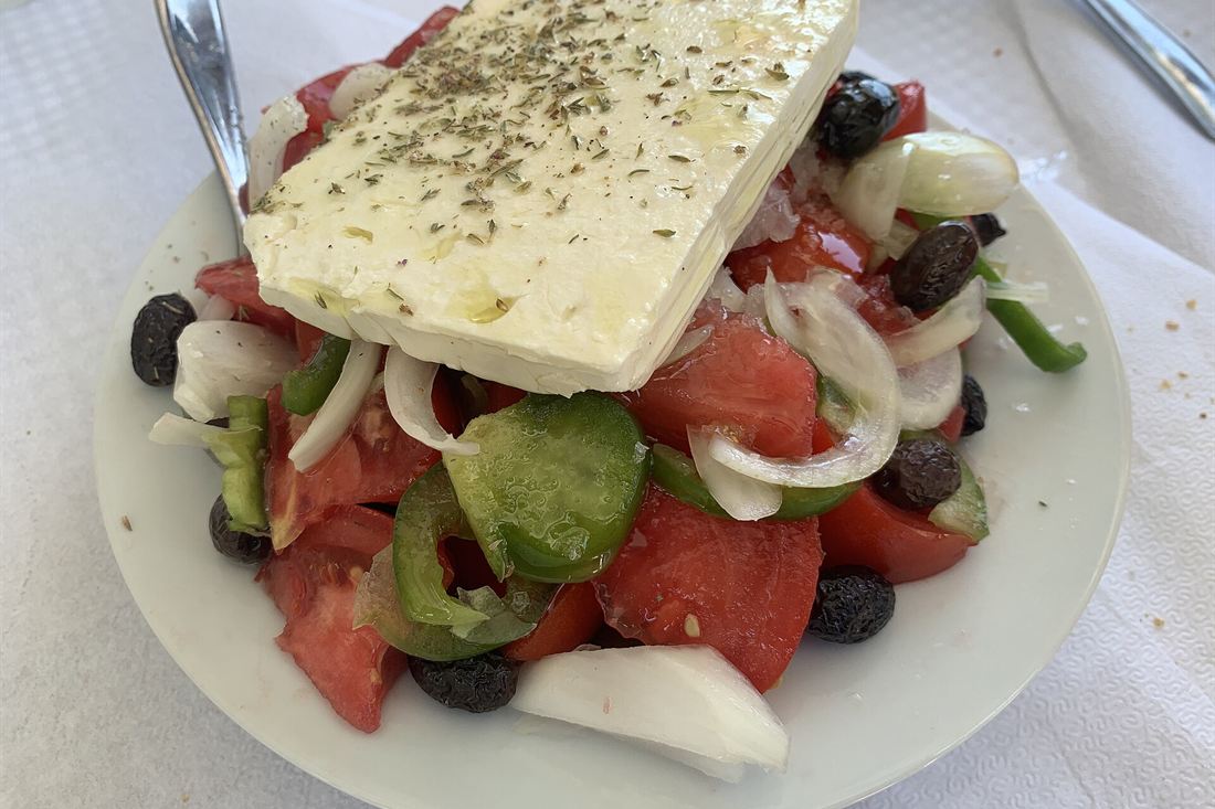 A Greek salad topped with a slab of feta, tomatoes, green peppers, onion and olives