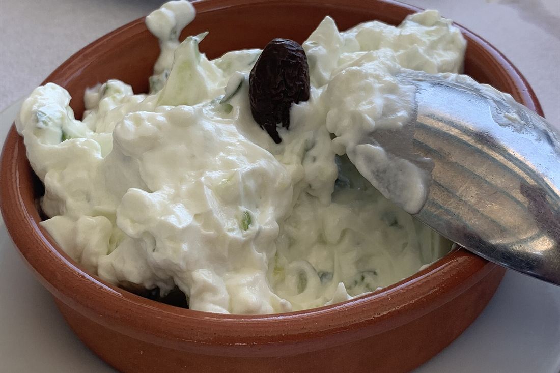 A clay bowl of tzatziki topped with a black olive