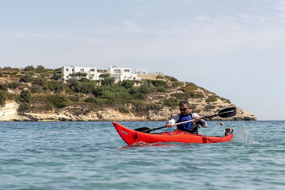 A paddler in a red sea kayak passes a green headland with white houses