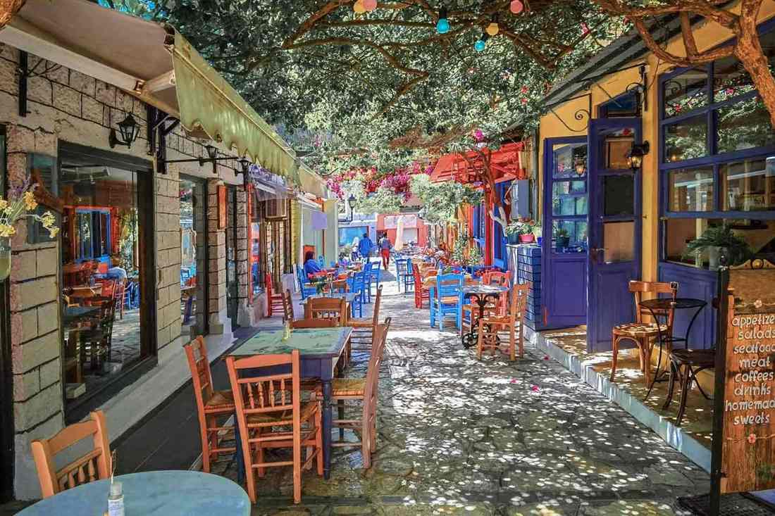 A colourful alley in the old town of Preveza with cafe tables under trees and flowers
