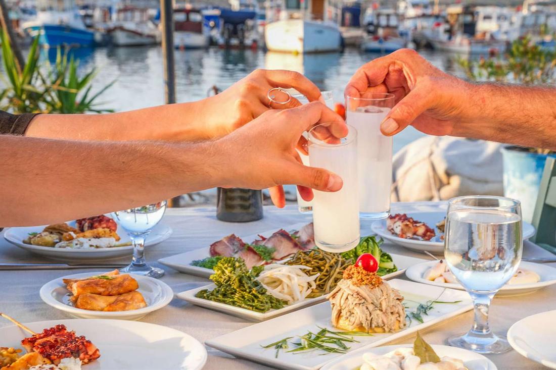 Glasses of ouzo raised over a table of seafood meze beside the harbour in Preveza