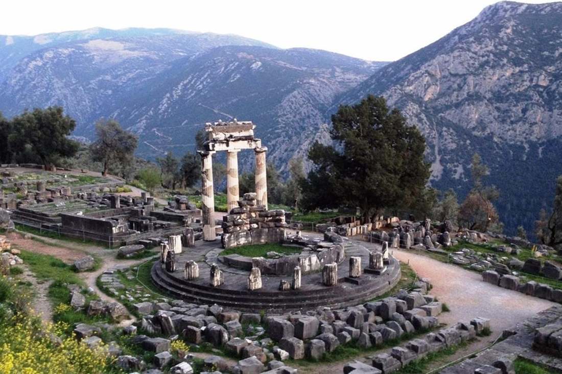 The round Tholos of Athena Pronaia at Delphi with three standing columns, below the cliffs and slopes of Mount Parnassus.