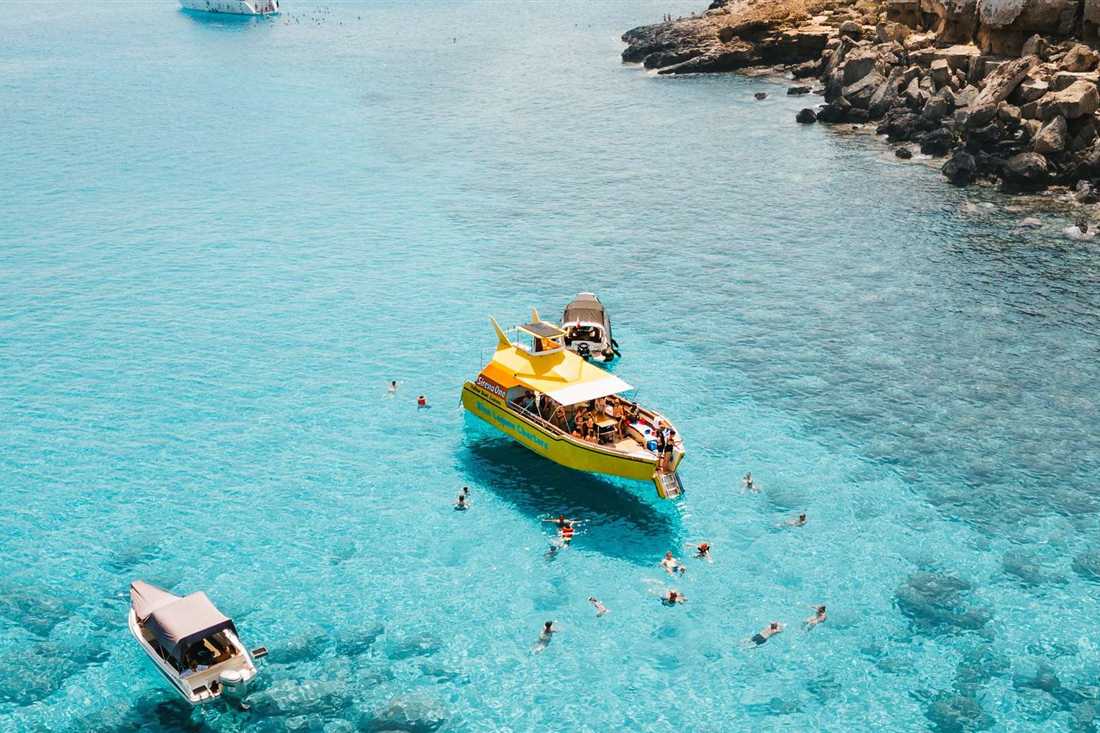 A yellow cruise boat anchored in the shallow turquoise Blue Lagoon at Cape Greco as guests swim around it