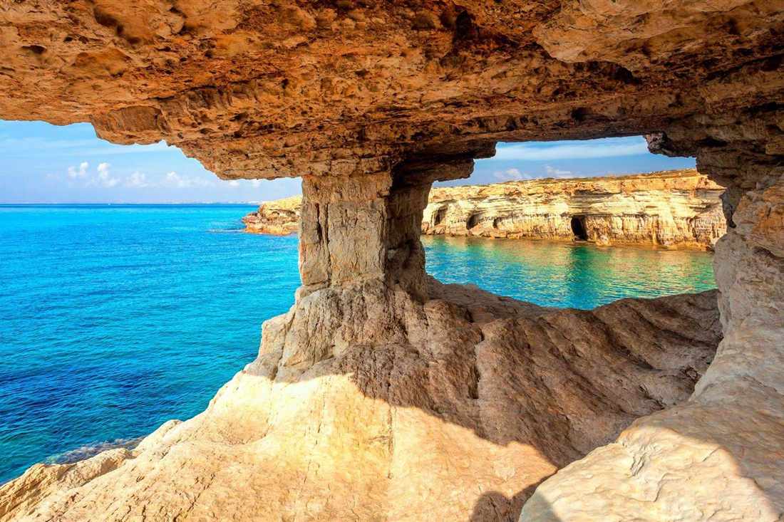 Rock window in the sea caves at Cape Greco framing turquoise water and a cliff coast