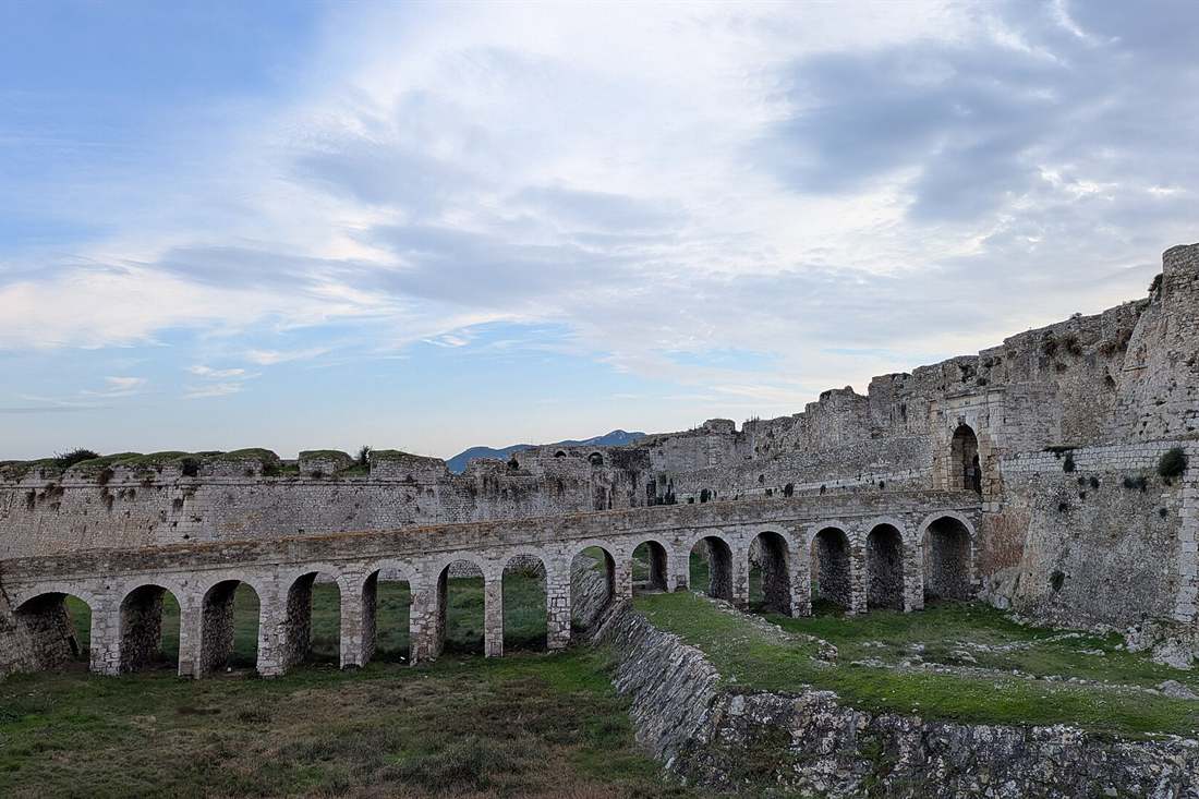 The arched bridge and long stone walls of Methoni Castle under a cloudy sky