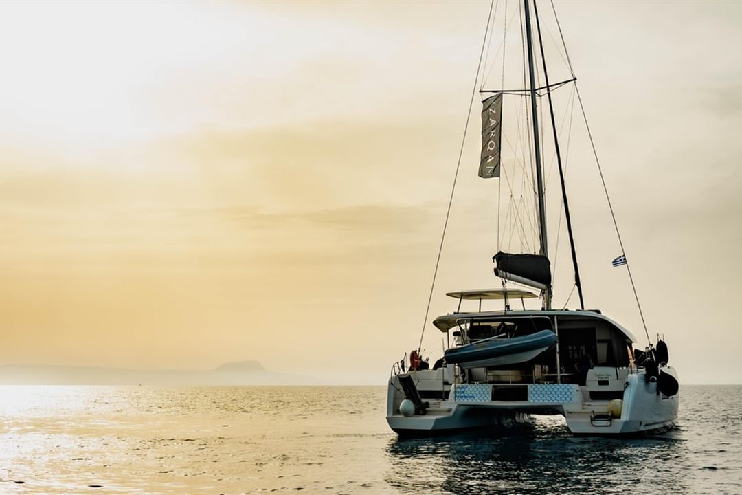 A sailing catamaran on calm water off Crete in the golden light of sunset.