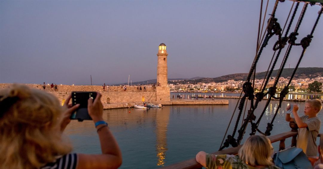 The stone lighthouse at the mouth of the Venetian harbour of Rethymno at dusk, seen from the deck of a boat.