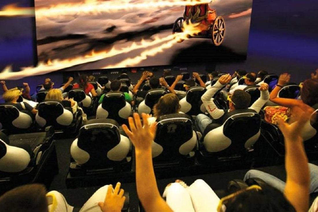 A cinema audience in 3D glasses raises their hands in moving seats as a flaming chariot crosses the screen at the Rhodes 9D history film.