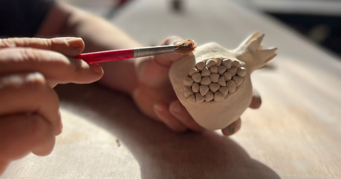 A brush adding paint to the seeds of an unglazed clay pomegranate in a Rhodes pottery class.