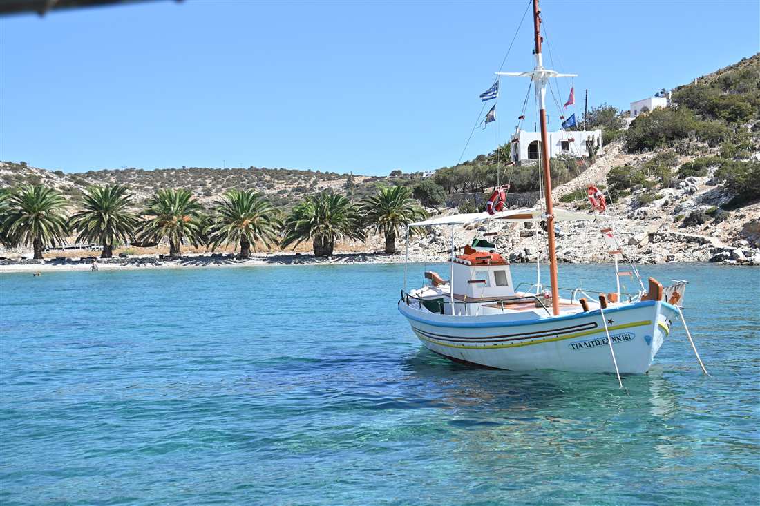 A traditional wooden boat moored in the clear water of Panermos bay, the departure point of the Rina Cave Naxos boat trips.