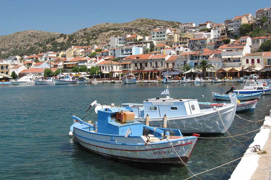 Fishing boats moored on the quay of Pythagorio harbour below the hillside houses on Samos, a stop on a Samos bus tour.