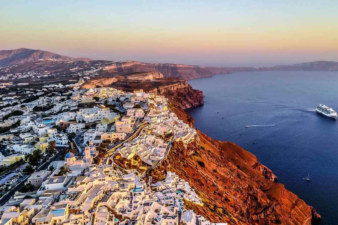 White houses of Fira along the rim of the red-brown Santorini caldera cliffs above the sea.