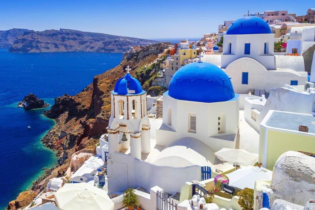 Blue-domed churches and white houses of Oia above the Santorini caldera and the Aegean Sea.