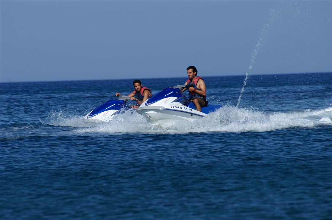 Two riders in life jackets on jet skis cutting across the blue Aegean, the kind of ride a Santorini jet ski rental or safari offers.
