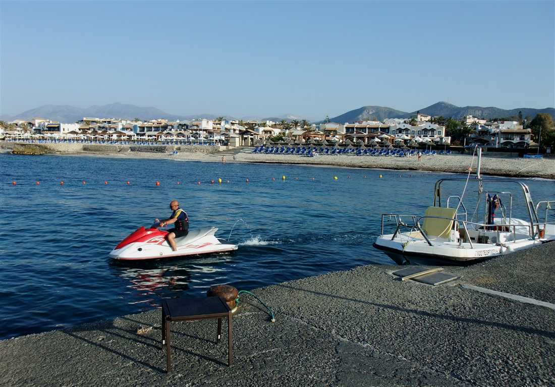 A rider on a jet ski leaving the jetty beside the buoy line of a swimming zone, the start of a Santorini jet ski ride from the beach.