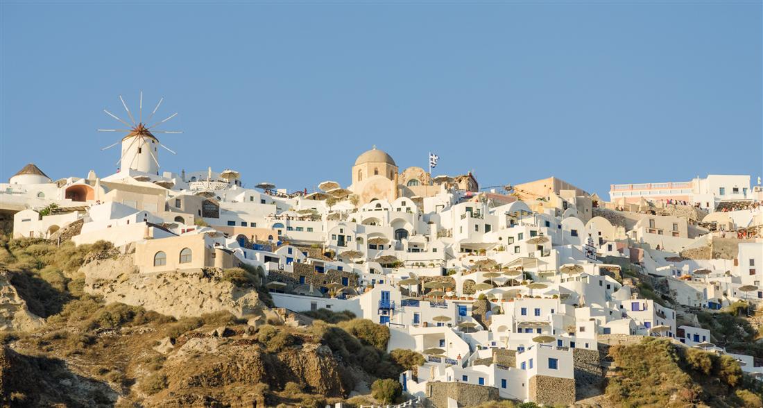 The white houses, domed church and windmill of Oia on the cliff of Santorini under a clear blue sky