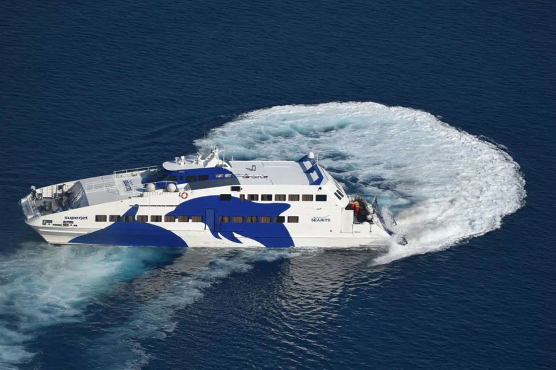 White and blue Seajets high-speed ferry turning on deep blue sea and leaving a curved white wake