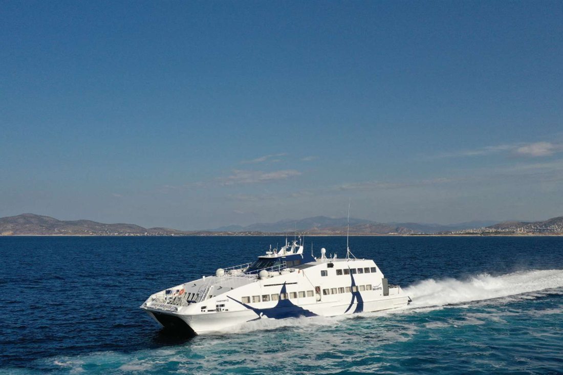 White Seajets fast ferry speeding across blue water with a hilly coastline behind it