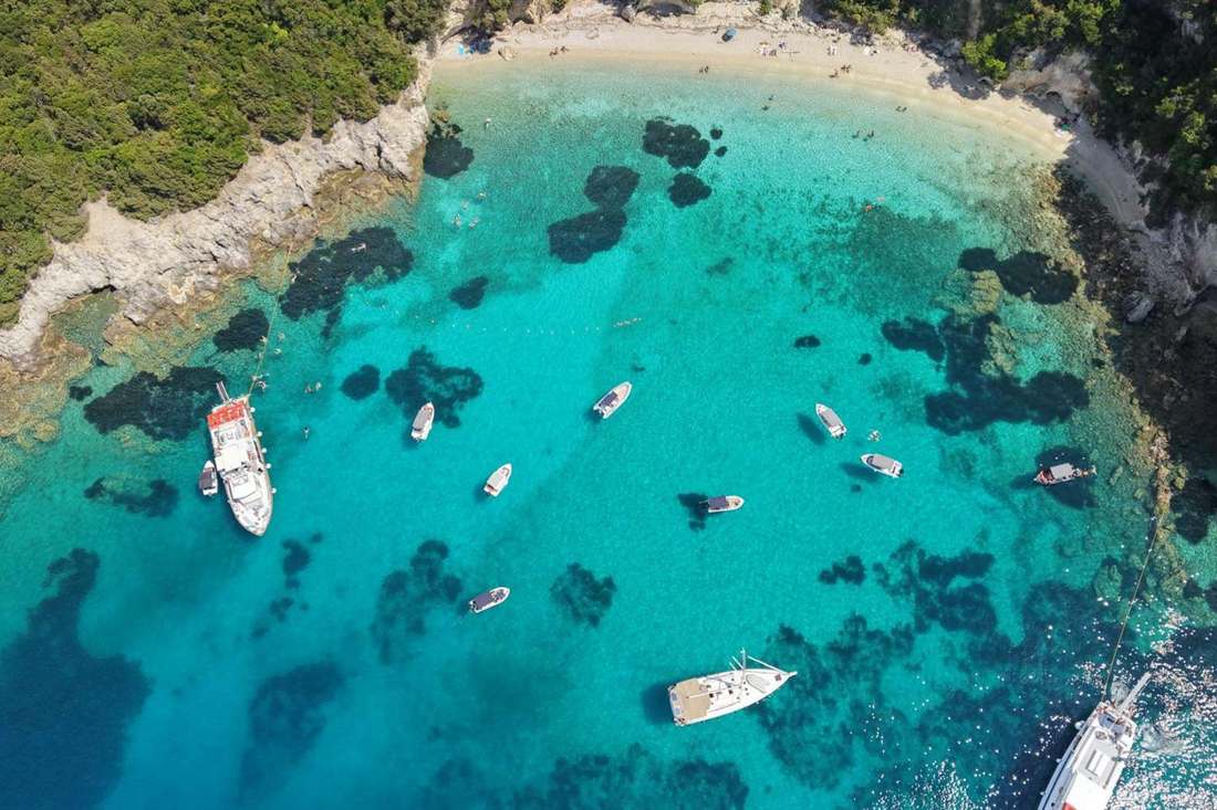 Aerial view of boats anchored in a turquoise bay with a sandy beach and forested rocky shores